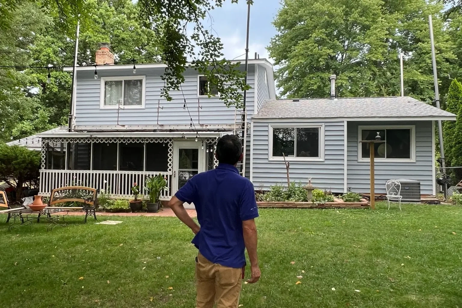 Homeowner standing in backyard observing siding and roofing replacement on two-story house with scaffolding