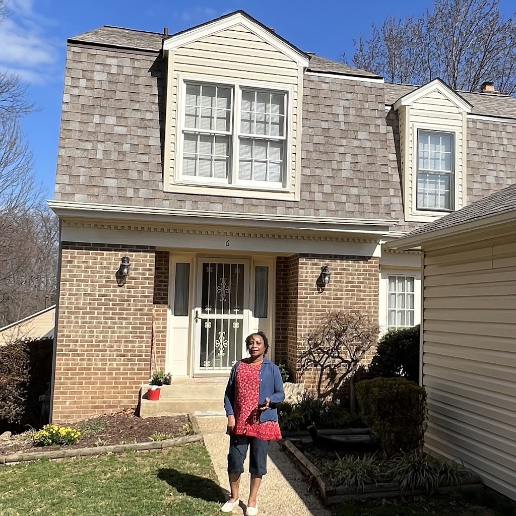Homeowner standing in front of a two-story brick and siding house with dormer windows and new roofing and siding replacement