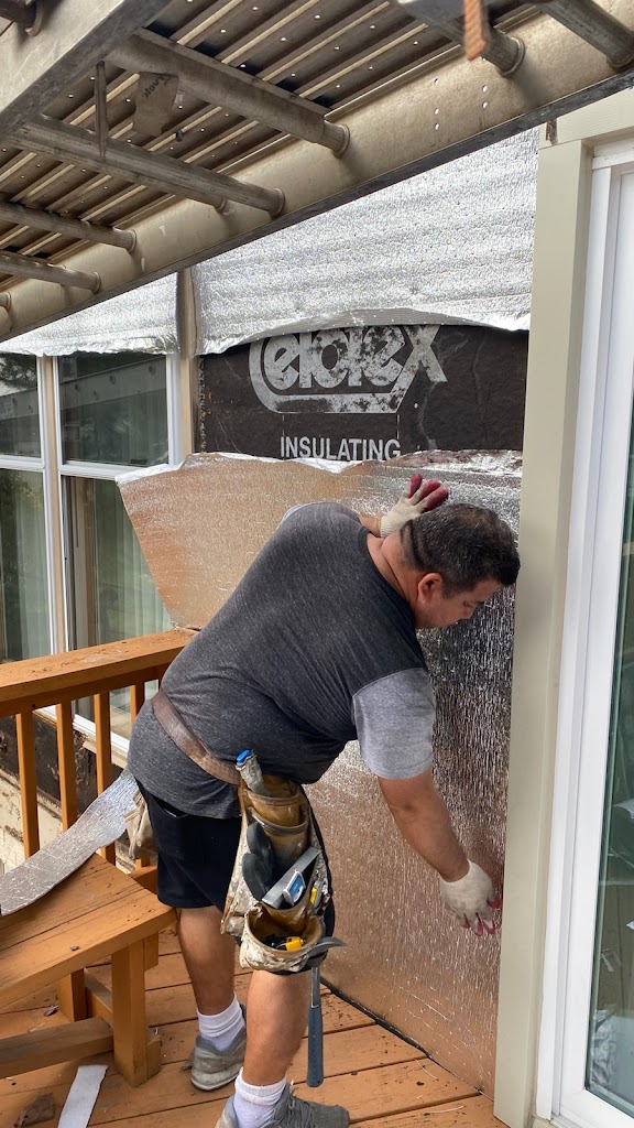 Worker installing reflective insulation wrap over exterior wall sheathing during siding replacement