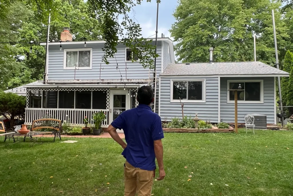 Homeowner standing in a backyard, observing siding and roofing replacement on a two-story house with scaffolding