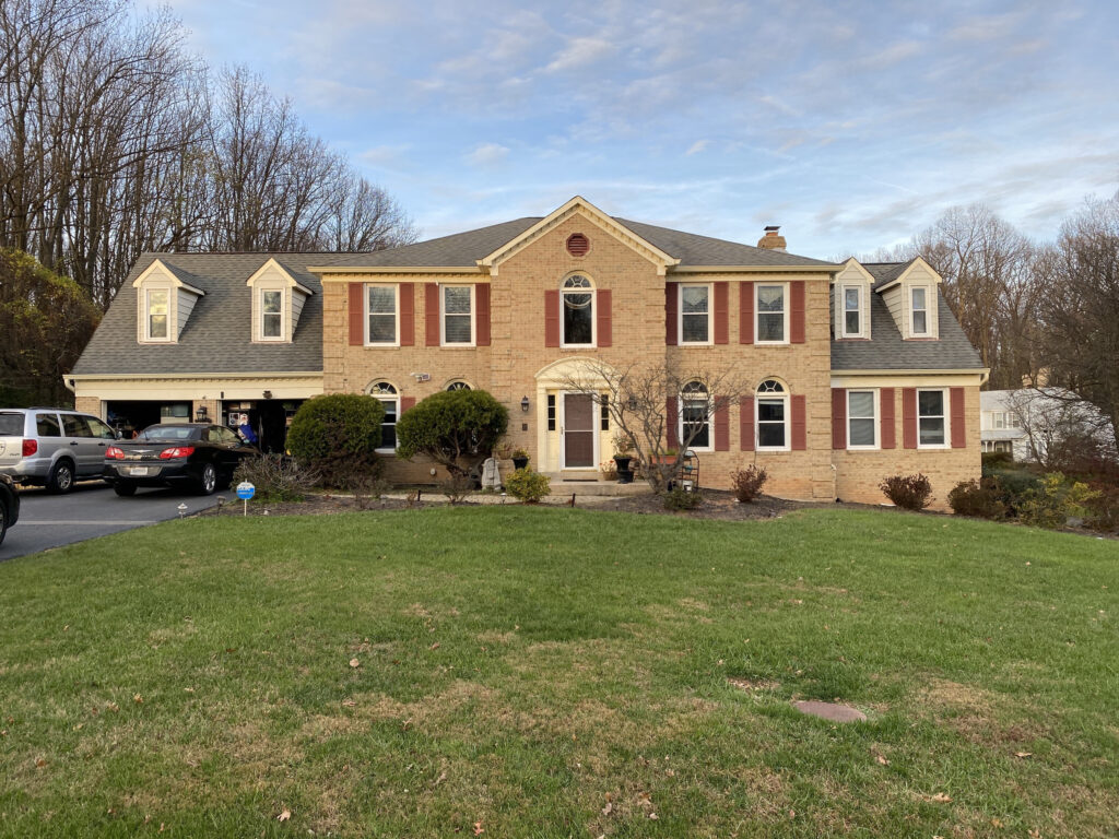 Large two-story brick house with dormer windows, red shutters, after a roof and siding replacement